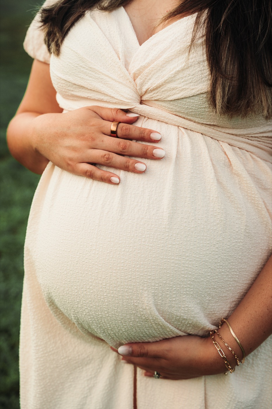 Hands gently resting on a baby bump in a cream dress