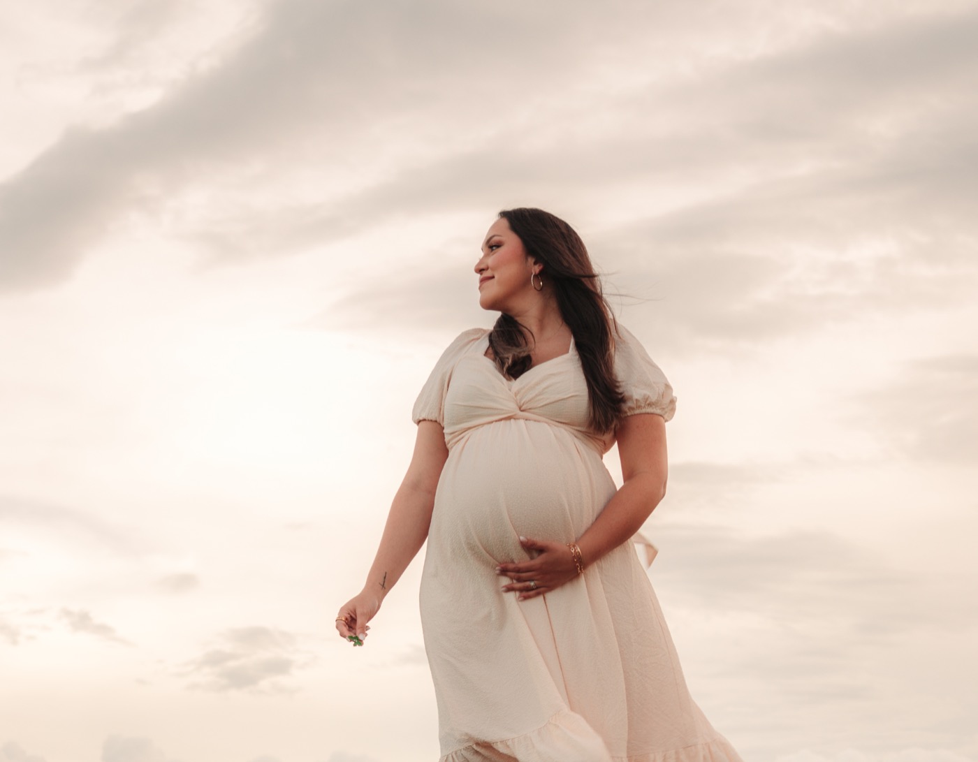 Maternity portrait in a cream dress beneath a soft evening sky