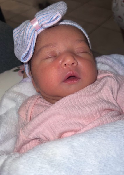 A newborn wearing a bow and wrapped in a pink blanket
